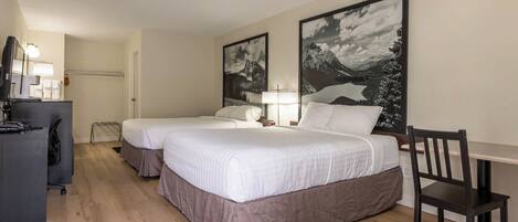 A hotel room with two beds, a desk, a chair, and large landscape paintings on the walls.