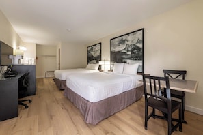 Habitación de hotel con dos camas, un escritorio, una silla y dos grandes cuadros de paisajes en la pared.