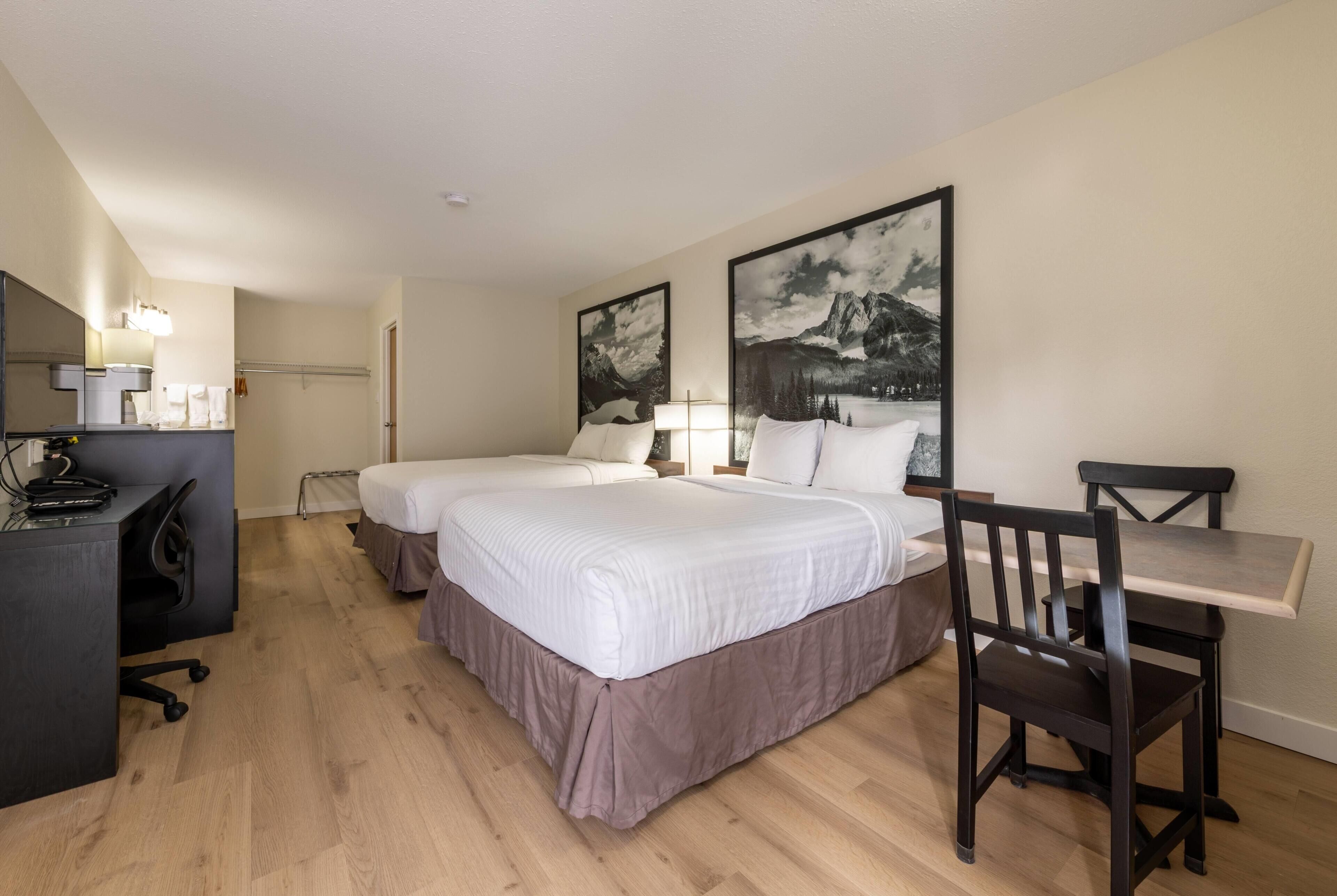 Una habitación de hotel con dos camas, un escritorio, una silla y una lámpara.