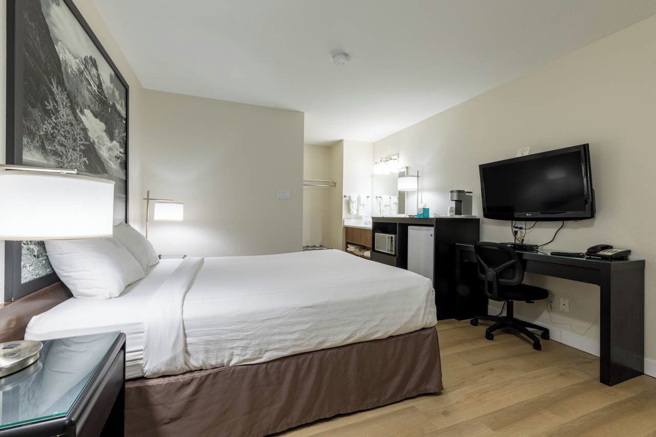 Una habitación de hotel con cama, escritorio, silla, televisión y un baño a la vista.