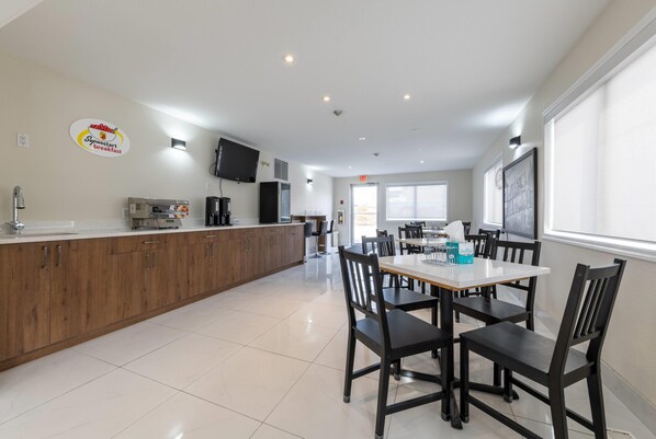 Een moderne keuken met een ontbijtbalk, een eethoek met een tafel en stoelen, en een groot raam dat voor natuurlijk licht zorgt.
