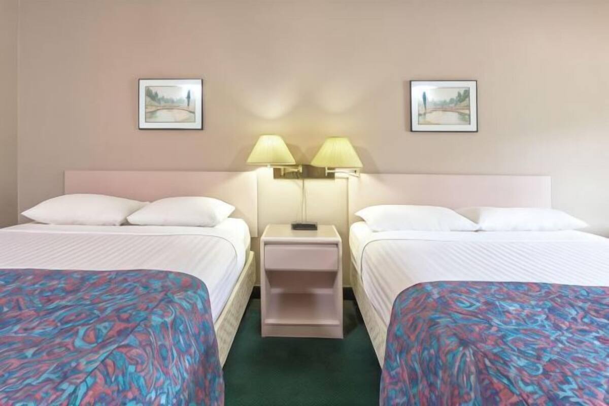 Een hotelkamer met twee bedden, een nachtkastje met lampen, en twee ingelijste foto’s aan de muur.