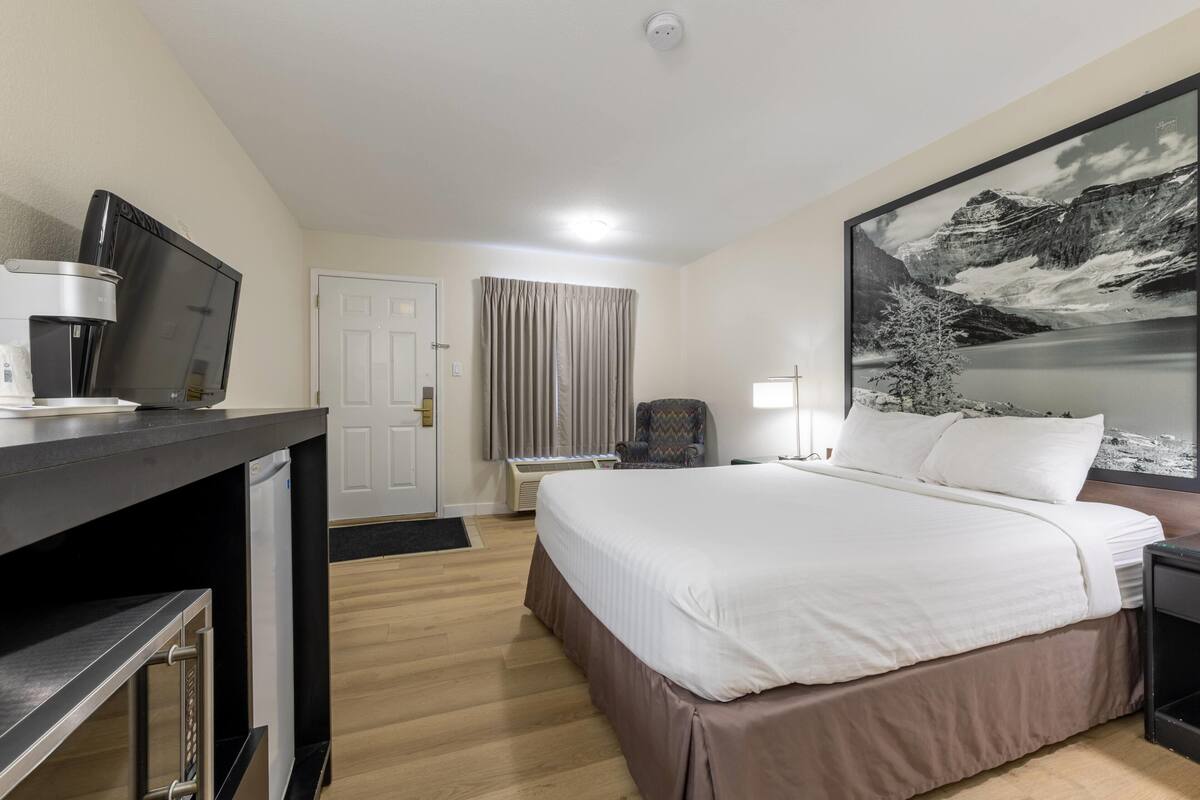 Een hotelkamer met een bed, een bureau met koffiezetapparaat, een stoel, een lamp en een groot beeld in een lijst aan de muur.