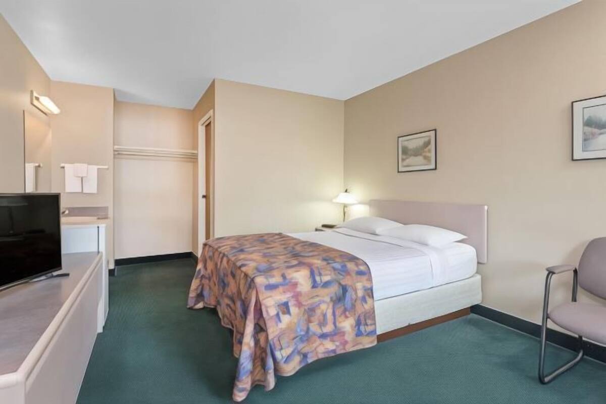 Een hotelkamer met een bed, een stoel, een televisie en een schilderij aan de muur.