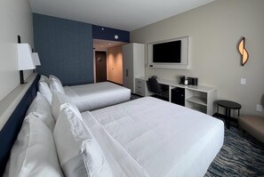 Ett hotellrum med två sängar, ett skrivbord, en stol, en tv och ett litet bord.