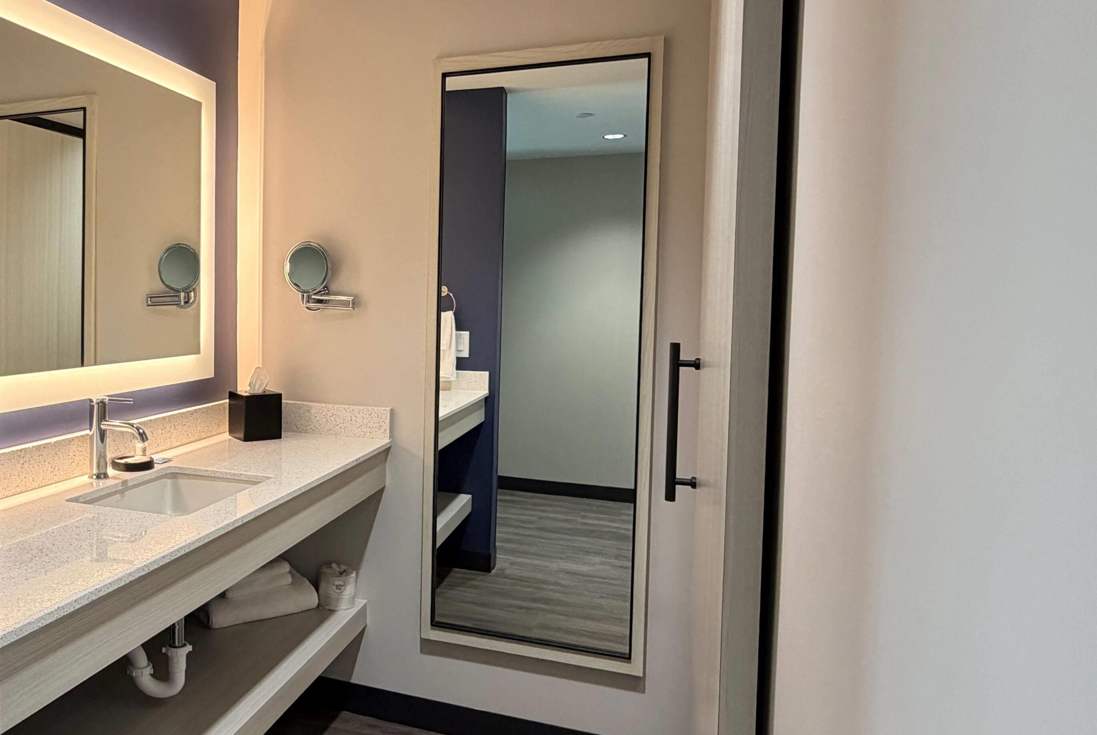 Un baño moderno con un espejo grande, dos espejos redondos, un lavamanos y un perchero para toallas.