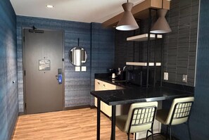 A modern kitchen with a black countertop, two pendant lights, and a wooden floor. - Sugar Creek Hotel, Trademark Collection By Wyndham (Hinton)