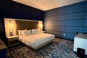 A hotel room with a large bed, two bedside lamps, a nightstand, a desk, and a patterned carpet. - Sugar Creek Hotel, Trademark Collection By Wyndham (Hinton)