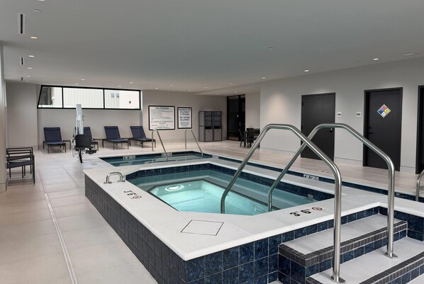 Un área de piscina interior moderna con señalización clara, una zona de estar y una escalera que lleva a un segundo nivel.