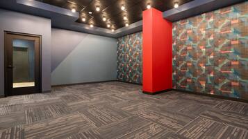 Un salón de conferencias con alfombra estampada, una pared de acento roja y una puerta con panel de vidrio satinado.
