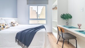 Une chambre avec un lit, une fenêtre, un bureau avec une chaise et une plante.