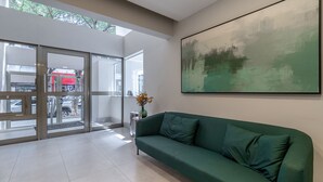Un intérieur moderne avec un canapé vert, un grand tableau abstrait et une porte en verre donnant sur l’extérieur.