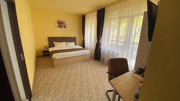 A hotel room with a bed, a desk, a chair, a nightstand, a lamp, and a painting on the wall.