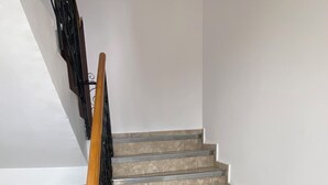 A staircase with a wooden handrail and metal balusters, leading to a landing with a white wall and a small picture frame.