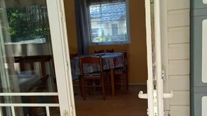 A room with a dining table and chairs, a window with blinds, and a door with a sign above it. - 🌞 Air-conditioned mobile home 6 pers - Camping 3⭐ avec piscine - Landes - dès 70€/nuit (Sainte-Eulalie-en-Born)