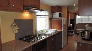 A compact kitchen with a gas stove, sink, microwave, and refrigerator. - 🌞 Air-conditioned mobile home 6 pers - Camping 3⭐ avec piscine - Landes - dès 70€/nuit (Sainte-Eulalie-en-Born)