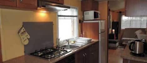 Cocina compacta equipada con estufa a gas, lavamanos, microondas y refrigerador.