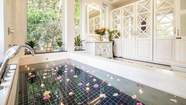 Une salle de bain avec un plancher en verre, des meubles blancs et une fenêtre donnant sur un paysage verdoyant.