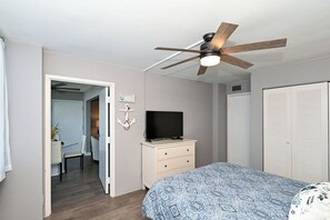 Ein Schlafzimmer mit einem Bett, einem Deckenventilator, einem Fernseher auf einer Kommode, einem Kleiderschrank und einer Tür zu einem anderen Raum.