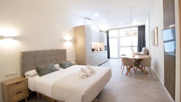 A modern bedroom with a bed, bedside table, and a dining area with a table and chairs. - Favara 1 by Concept Flats (Valencia)