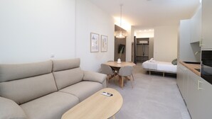 A modern living room with a sofa, a dining table, and a kitchen area. - Favara 1 by Concept Flats (Valencia)