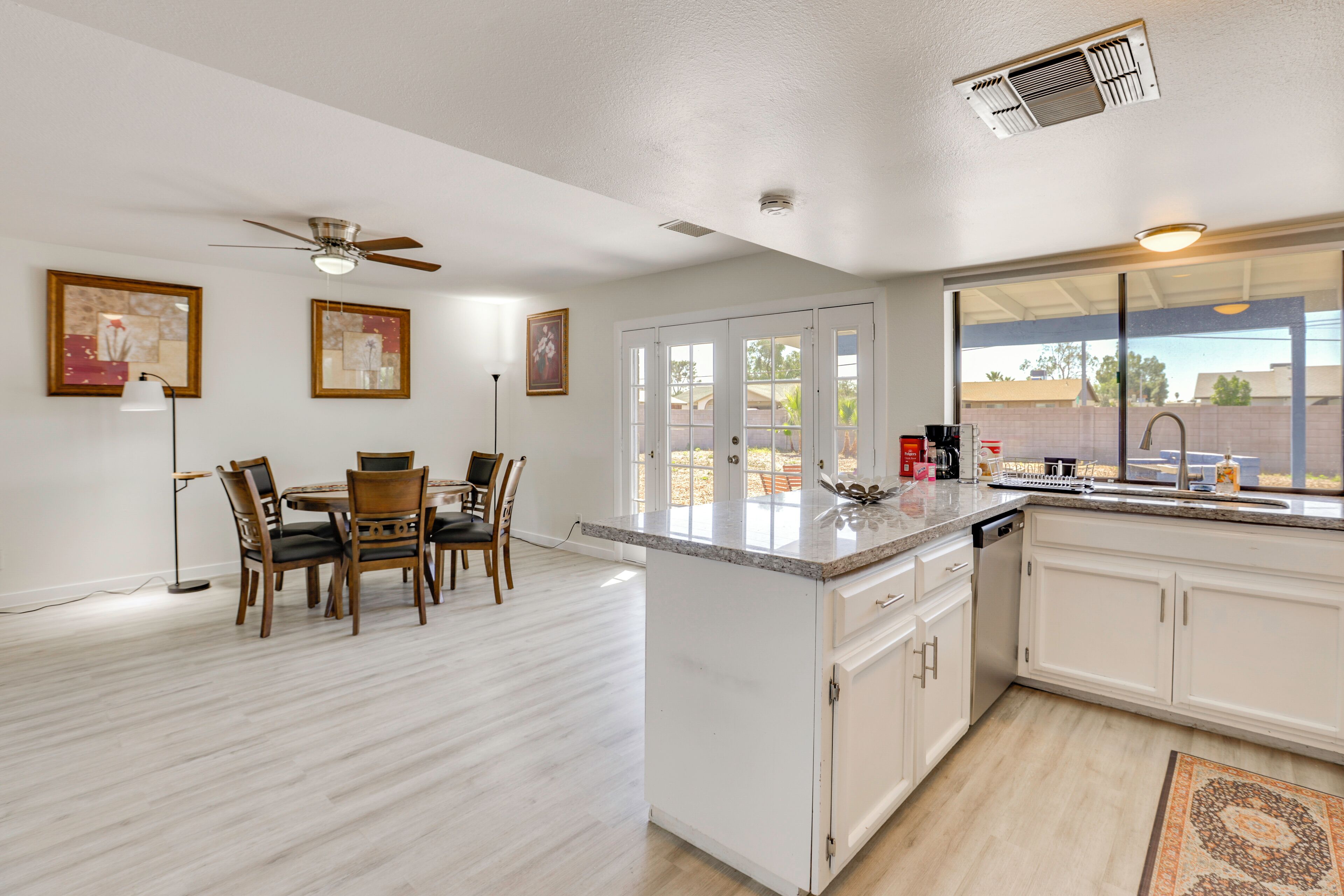 Une cuisine moderne avec des meubles blancs, un coin repas doté de chaises en bois et un ventilateur de plafond.