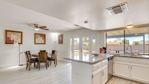 A modern kitchen with white cabinetry, a dining area with wooden chairs, and a ceiling fan.