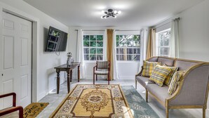 Ein Wohnzimmer mit einer Couch, einem Sessel, einem Fernseher und einem großen Fenster mit Vorhängen.