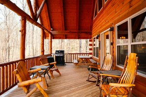 A wooden deck with outdoor seating, a grill, and a view of the surrounding forest.