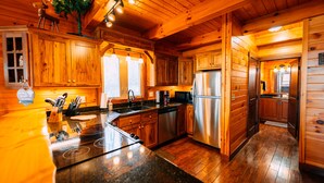 Interieur van een houten hutje met een keuken, voorzien van een roestvrijstalen koelkast, houten kastjes en een granieten aanrecht.