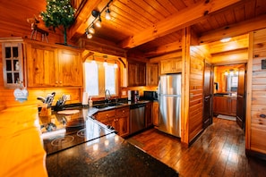 A wooden cabin interior with a kitchen featuring a stainless steel refrigerator, wooden cabinets, and a granite countertop.