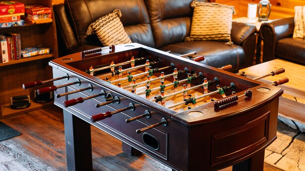 Een tafelvoetbaltafel in een kamer met een leren bank en houten vloer.