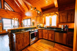 A wooden cabin interior with a kitchen featuring a stove, oven, and dishwasher. - Serenity Now | Hocking Hills, Covered Hot Tub (Logan)