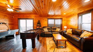 A wooden cabin interior with a pool table, leather sofa, and a fireplace.