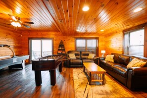 A wooden cabin interior with a pool table, leather sofa, and a fireplace.