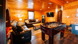 A cozy room with a leather sofa, a foosball table, a television, and a fireplace.