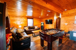 A cozy room with a leather sofa, a foosball table, a television, and a fireplace.