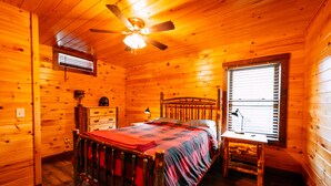 Een slaapkamer in een houten blokhut met een bed, een bureau, een plafondventilator en een raam.