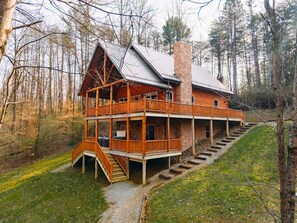 A two-story log cabin with a balcony, a stone chimney, and a staircase leading to the upper level.