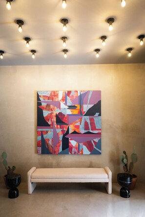 Una habitación con un banco, un cuadro abstracto y colorido, e iluminación en el techo.