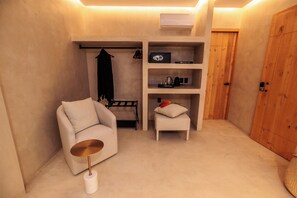 Une pièce de taille modeste, comprenant un canapé, une petite table, une étagère avec quelques objets, un porte-manteau et une porte en bois.