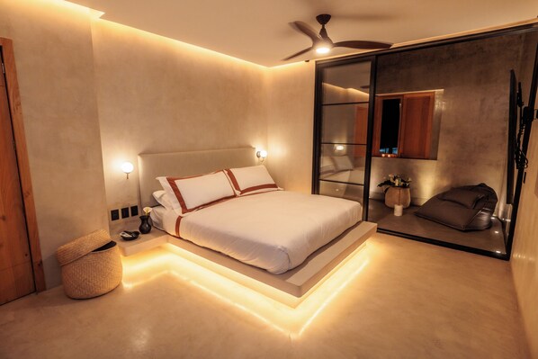 Une chambre à coucher moderne avec un lit, des lampes de chevet, un ventilateur de plafond et un grand miroir.