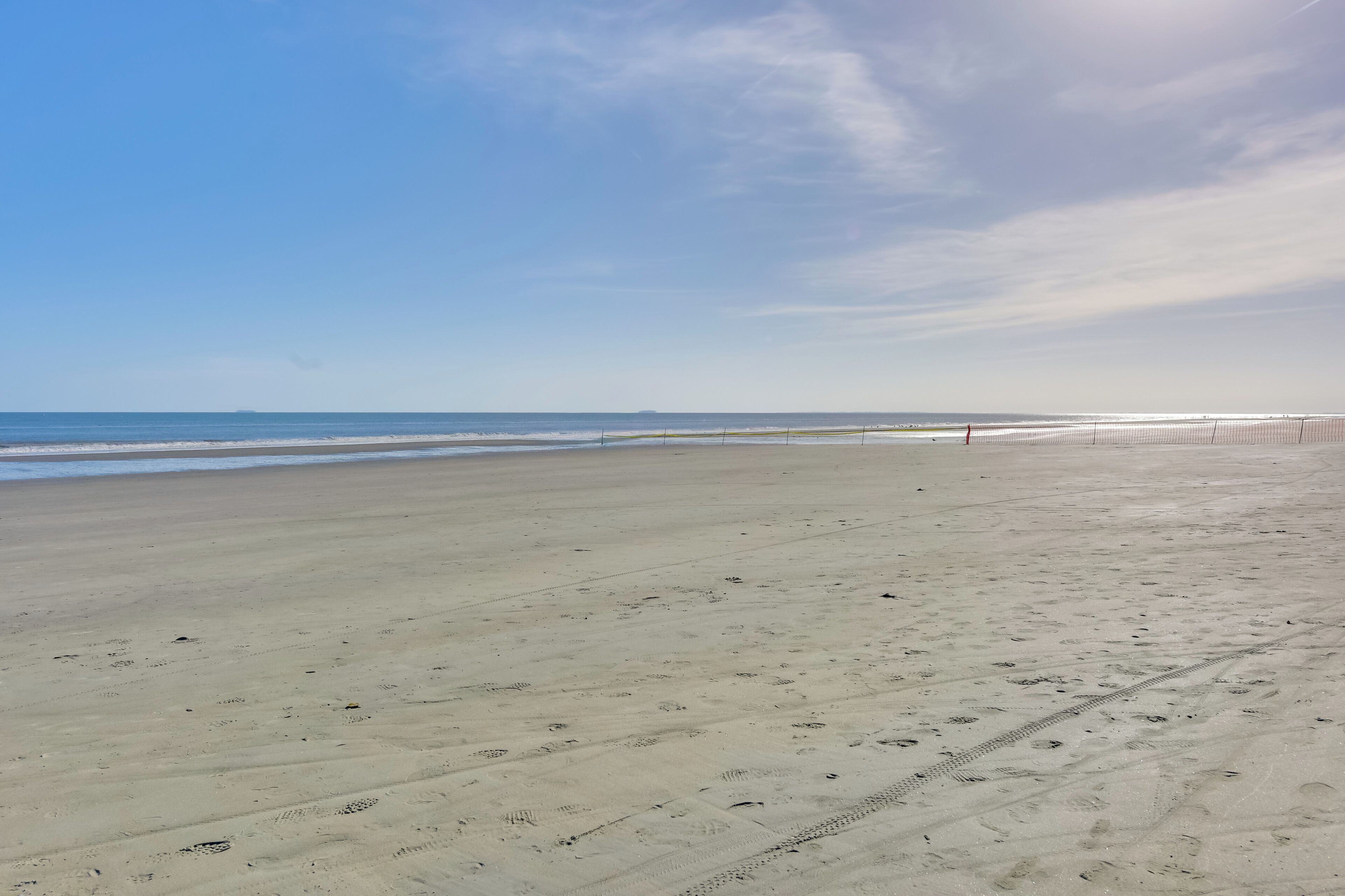 Ampia spiaggia sabbiosa, con impronte e cielo sereno.