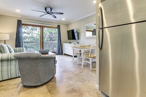 A modern kitchen with a stainless steel refrigerator, a dining area with white chairs, a gray sofa, and a ceiling fan. - Steps to Shore & Restaurants: Coligny Beach Gem! (Hilton Head Island)