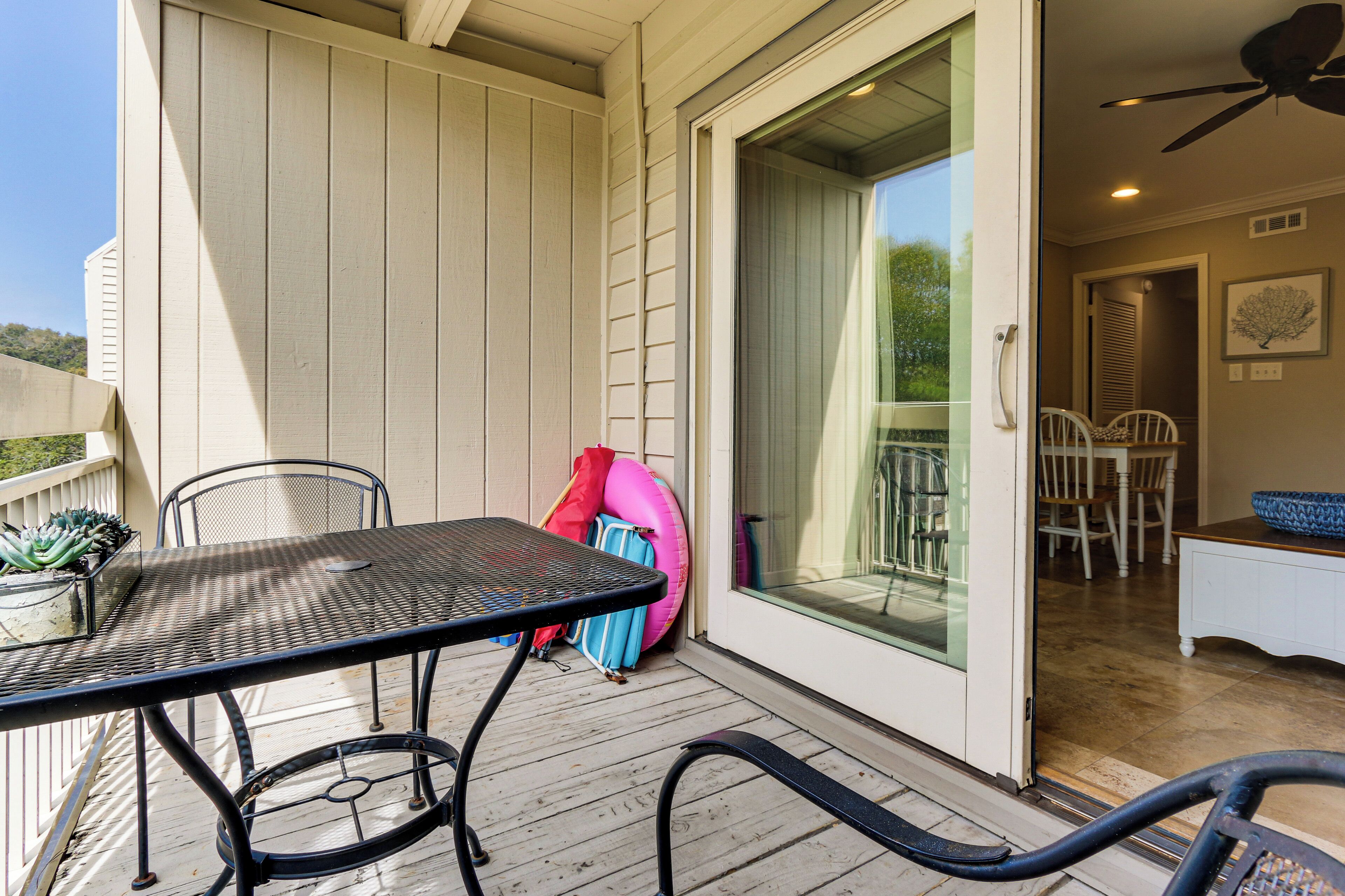 A covered outdoor area with a table and chairs, a sliding glass door leading to an interior space with a ceiling fan, and a view of the outdoors.