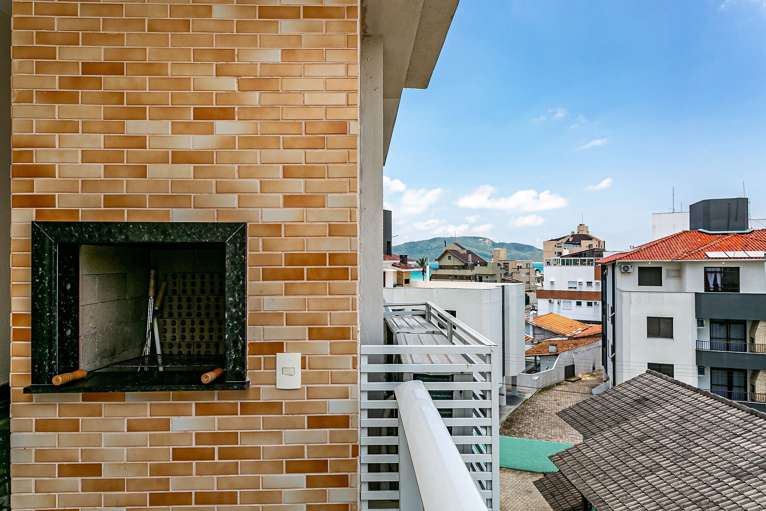 A brick wall with a fireplace, a balcony railing, and a view of neighboring buildings.