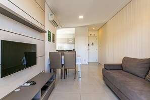 Ein Wohnzimmer mit Flachbildfernseher, einer Couch, einem Esstisch mit Stühlen und einer Küchenzeile im Hintergrund.