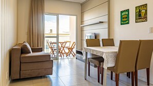 Ein modernes Wohnzimmer mit einer Couch, einem Esstisch, Stühlen und einer Schiebeglastür, die auf einen Balkon führt.
