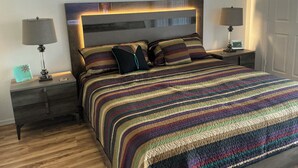 Un letto rifatto con cura, coperto da una tenda a righe, due comodini con lampade e una testiera con illuminazione integrata.
