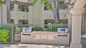 Un'area esterna recintata con due barbecue, un cartello con le istruzioni per il grill a gas e un edificio sullo sfondo con diversi balconi.
